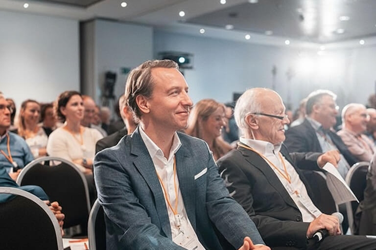 Publikum sitzt in einem Konferenzraum und hört einer Präsentation zu; links oben ist das Cellex‑Logo zu sehen.